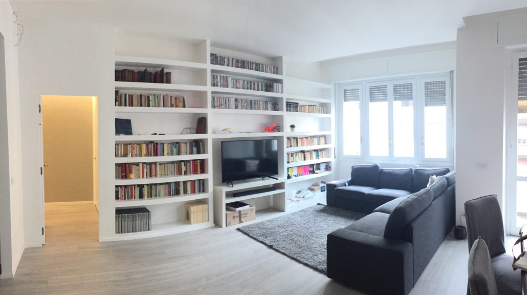 Interior Design_02-PF-Archistudio Soggiorno con libreria bianca su misura a tutta parete e divano angolare grigio