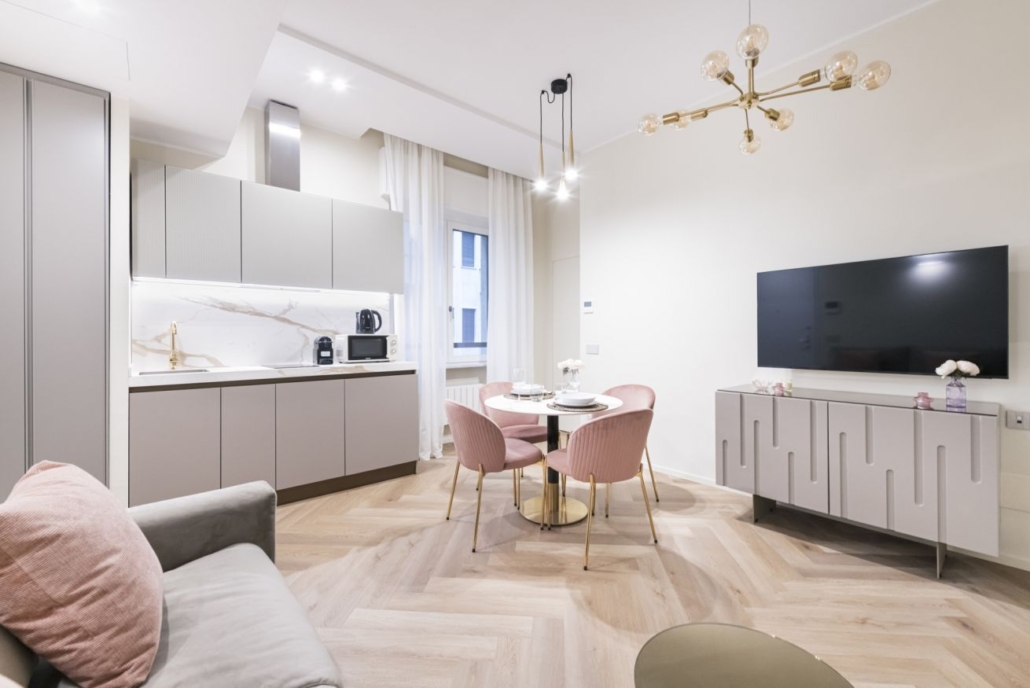 Centro Storico di Milano_03-PF-Archistudio Zona giorno con cucina a vista, tavolo rotondo con sedie rosa e lampadario a bracci