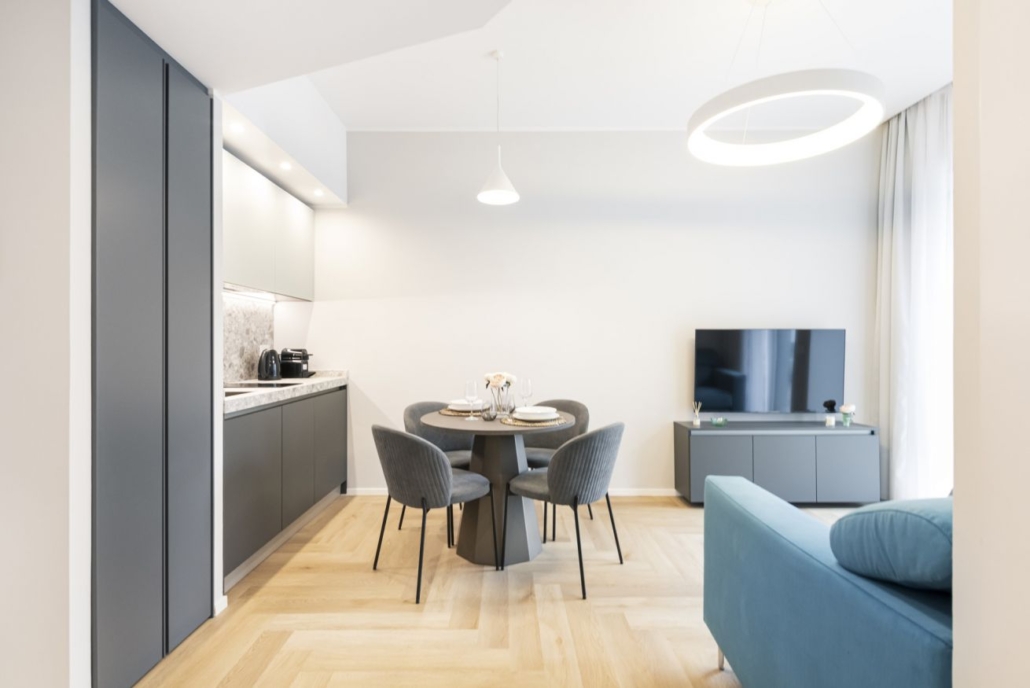 Centro Storico di Milano_04-PF-Archistudio Soggiorno con cucina, tavolo da pranzo rotondo, divano azzurro e lampada ad anello