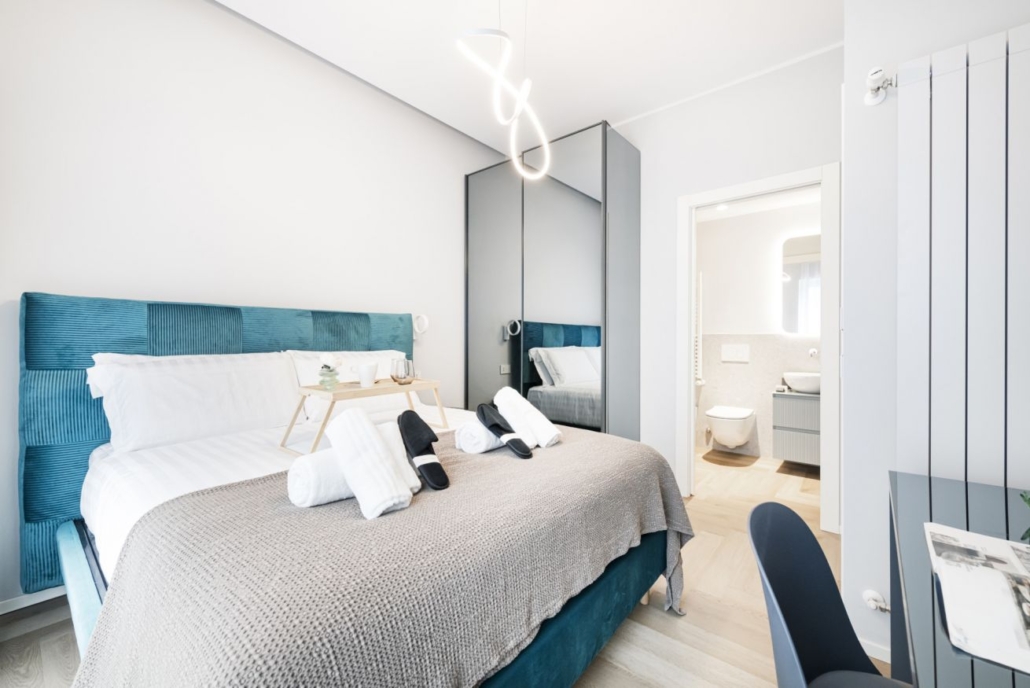 Centro Storico di Milano_06-PF-Archistudio Camera da letto con testiera blu petrolio e il bagno visibile sullo sfondo