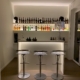 Angolo bar con banco illuminato, tre sgabelli e mensole retroilluminate con bottiglie