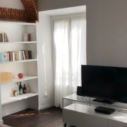 Soggiorno con libreria bianca, arco di mattoni a vista e televisore su mobile basso