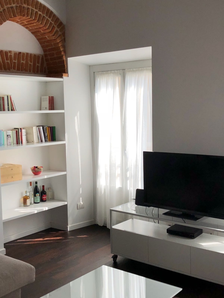 Appartamento Porta Garibaldi_03-PF-Archistudio Soggiorno con libreria bianca, arco di mattoni a vista e televisore su mobile basso